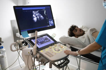 A patient lies on an examination table receiving an ultrasound scan with a sonographer operating the equipment. - ADSF53695