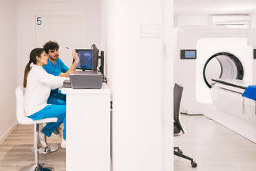 Two healthcare workers operate a magnetic resonance imaging (MRI) system in a modern medical clinic. - ADSF53702