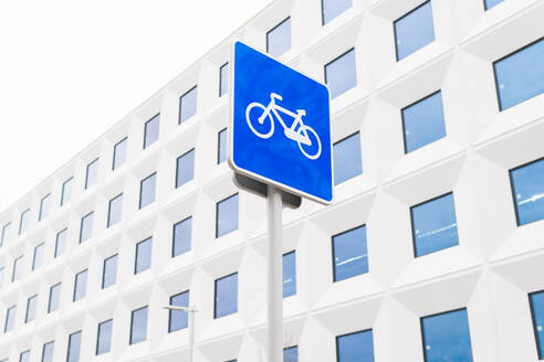 A bicycle lane sign prominently displayed in front of a modern building with a geometric facade, highlighting urban cycling infrastructure - ADSF53711