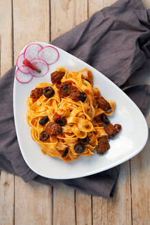 Top view of fettuccine topped with a rich tomato sauce, black olives, and sundried tomatoes, garnished with sliced radishes on a white plate - ADSF53718