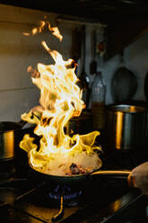 A dramatic shot of a skillet on a stove with a blazing fire engulfing the food, demonstrating a flambé cooking method - ADSF53719