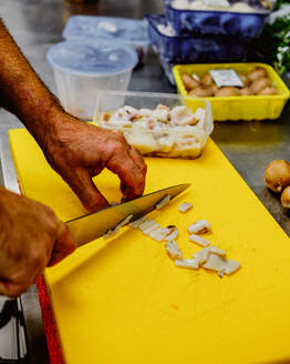 Anonymous chef is slicing mushrooms on a vibrant yellow cutting board, with kitchen containers in the background - ADSF53720