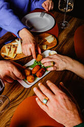 A group of friends reaches for delicious tapas on a plate at a warm and friendly dinner gathering, sharing food and enjoying each other's company - ADSF53726