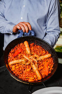 A person holds a pan full of rich seafood paella, vibrant with prawns and spices - ADSF53728