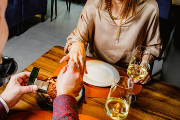 A couple enjoys a romantic dinner as one person proposes with a ring box, while champagne glasses and elegant plates complement the scene - ADSF53730