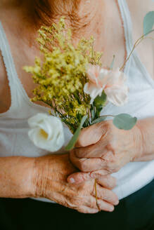 Close-up of elderly hands holding a small bouquet with a gentle touch - ADSF53756