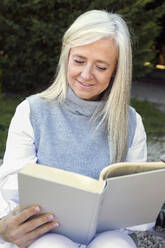 Serene woman in her 50s engrossed in reading a book, exemplifying a relaxed lifestyle moment - ADSF53762