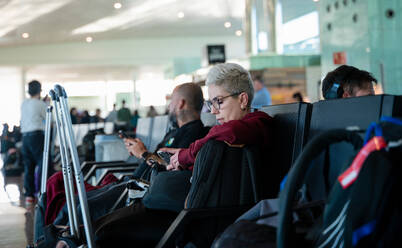 Woman seated at airport lounge looking at phone, waiting for boarding while traveling in Malaysia. - ADSF53773