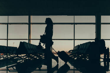 Side view of an anonymous woman is silhouetted against a bright airport window, indicating a travel concept with a back view of her figure, portraying the anticipation of embarking on a journey. - ADSF53774