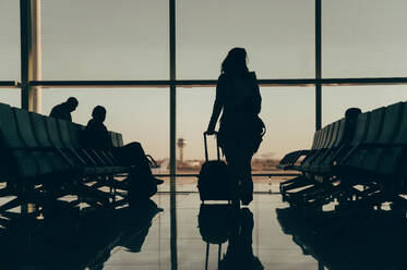 Silhouette of unrecognizable woman traveler with luggage at an airport in Malaysia, showcasing the concept of travel, with a back view in an anonymous setting. - ADSF53776