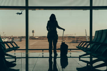 Silhouette of unrecognizable woman traveler with luggage at an airport in Malaysia, showcasing the concept of travel, with a back view in an anonymous setting. - ADSF53777