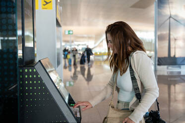 A woman is checking in at an airport self-service kiosk, getting ready for her flight to Malaysia. - ADSF53779