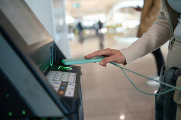 Back view of a woman using a contactless payment system at an airport kiosk, exemplifying modern travel convenience. - ADSF53780