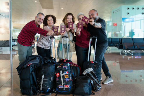 A cheerful group of four adults friends at an airport, proudly displaying their passports before a flight, indicating excitement for their journey ahead. - ADSF53781