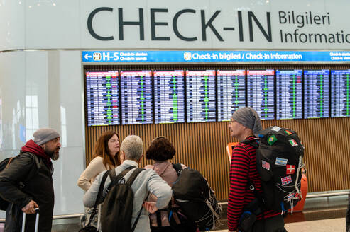 Group of travelers checking flight information at airport with a focus on a woman with a backpack. - ADSF53785