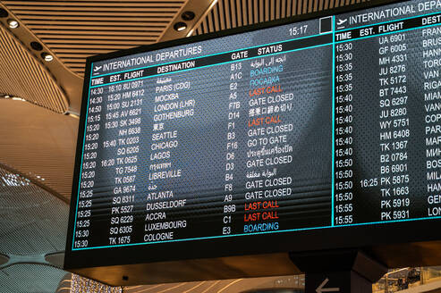 An illuminated airport departures board shows international flight times, destinations, and statuses. - ADSF53786