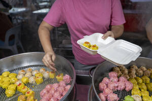 Cropped unrecognizable woman in a pink shirt is serving various colorful dim sum from a steaming street stall in Malaysia. - ADSF53789