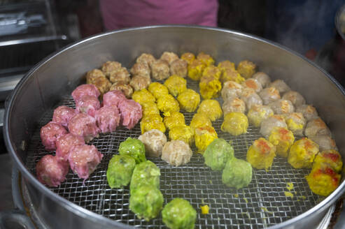 Steamed multi-colored dumplings showcased in a street food market in Malaysia, with steam rising as they cook. - ADSF53790