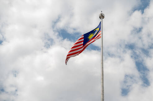 The Malaysian flag soars on a tall mast with a cloudy blue sky as the backdrop, symbolizing national pride. - ADSF53792