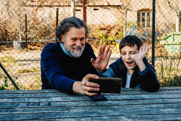 A grandfather and grandson share a joyous moment during a video call with family members outside - ADSF53811