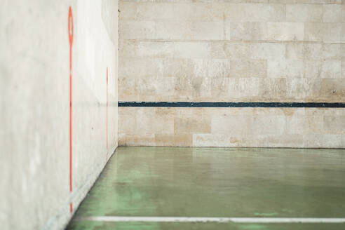 A view of an empty outdoor handball court with distinctive red lines on a concrete wall and a black line on the ground, showing signs of wear and tear. - ADSF53840