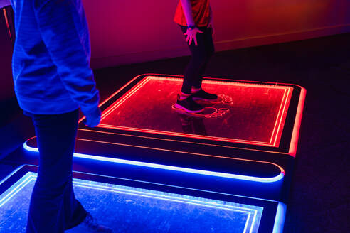 Two anonymous people standing on an interactive LED floor game with glowing neon outlines in a dark arcade setting - ADSF53844