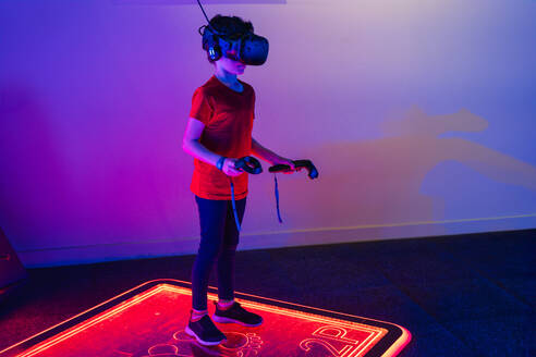 Anonymous kid engaged in a virtual reality simulation, standing on a neon-glowing interactive platform - ADSF53845
