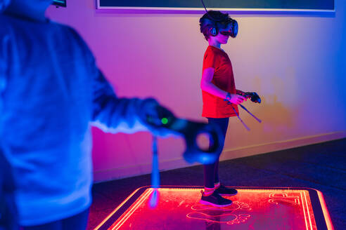 Anonymous players in VR headsets engaging with virtual reality games on a glowing platform in a neon arcade room - ADSF53848