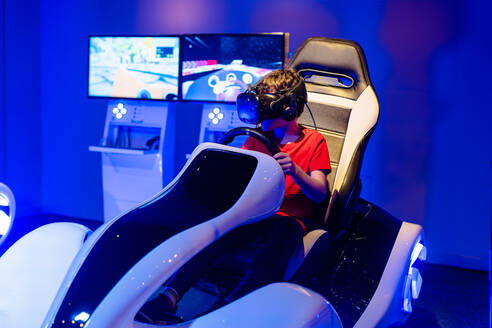 A child gamer is engrossed in a virtual racing experience, using a VR headset while seated in a modern simulator - ADSF53850