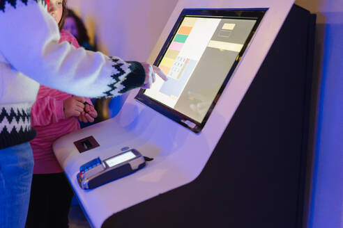 Anonymous customer touching a digital screen at a checkout kiosk with a payment terminal in a retail setting - ADSF53852