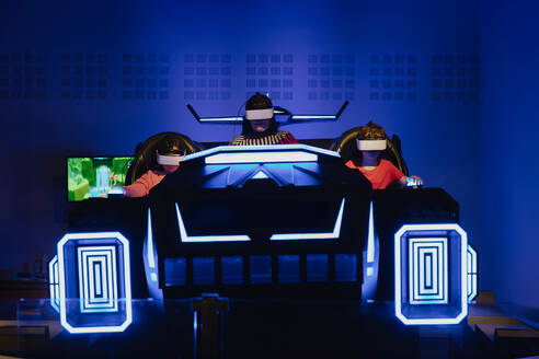 Three people are fully engaged in a virtual reality simulation, each wearing VR headsets and sitting in futuristic simulator pods - ADSF53857