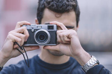 Young man capturing a moment with a vintage camera, focus on camera with blurred background - ADSF53944