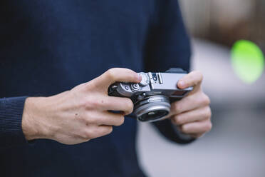 Close-up of a man's hands adjusting the settings on a vintage camera with a blurred urban background - ADSF53945