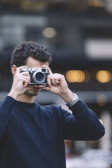 Young photographer capturing a photo with a retro style camera, bokeh lights in the background - ADSF53946