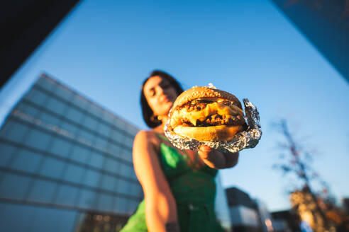 A woman in urban Madrid showcases a juicy burger against the backdrop of the Four Towers business area. - ADSF53954