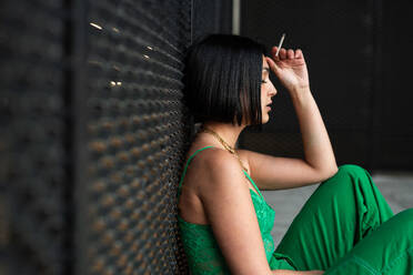 Side view of chic woman in a stylish green outfit poses thoughtfully against a textured wall in Madrid, exuding urban sophistication near the Four Towers area. - ADSF53964