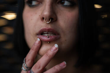 Close-up shot of a young woman with nose and lip piercings deep in thought, set against a blurred backdrop hinting the urban style of Madrid's Four Towers Business Area. - ADSF53966