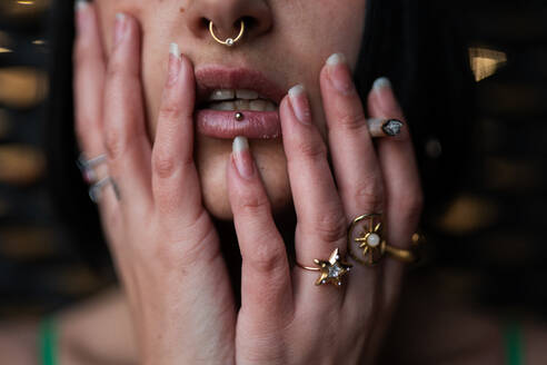 A detailed close-up of cropped unrecognizable a woman's pierced lower lip and ornate rings, reflecting a modern urban style. - ADSF53967