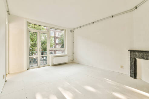 Spacious and well-lit empty room featuring a large window front, balcony door, and a vintage fireplace. - ADSF53986