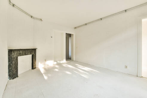 An empty room featuring pristine white walls, a classic marble fireplace, and beams of sunlight pouring in from windows. - ADSF53987