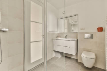 A contemporary bathroom featuring a glass shower, sleek sink vanity, and wall-mounted toilet in a bright and neutral color scheme. - ADSF53993