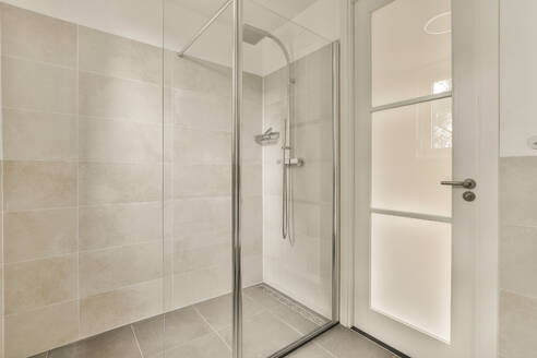 A clean, modern bathroom featuring a glass shower cubicle with beige tiled walls. - ADSF53994