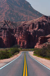 Winding road leading through the striking red rock formations of Los Castillos in the desert landscape of northern Argentina, with a clear blue sky overhead - ADSF54000