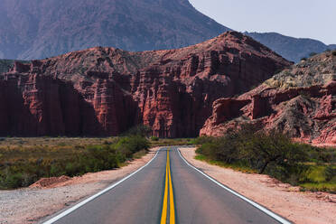 A curving road meanders through the deep red canyons of Los Castillos, contrasting with vibrant green shrubbery under the expansive blue sky - ADSF54001