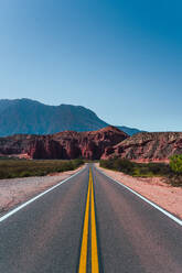 Straight road stretching towards red rock formations under a vast blue sky in the Los Castillos area of northern Argentina - ADSF54002