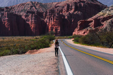 Anonymous traveler pausing by the roadside to admire the majestic red cliffs of Los Castillos under the Argentine sun - ADSF54003