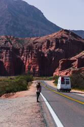 Anonymous person walking along the roadside with a van driving on a winding road through the red canyons of Los Castillos - ADSF54004