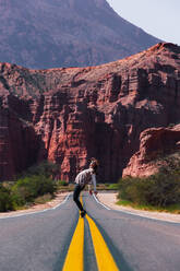 Individual playfully balancing on the road's yellow lines with the striking red formations of Los Castillos in the background - ADSF54006