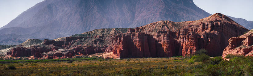 Expansive view of the red rock formations of Los Castillos with a towering mountain range in the background and lush brush in the foreground - ADSF54008