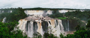 Panoramic view of the Iguazu Falls surrounded by lush greenery and mist under an overcast sky. - ADSF54020